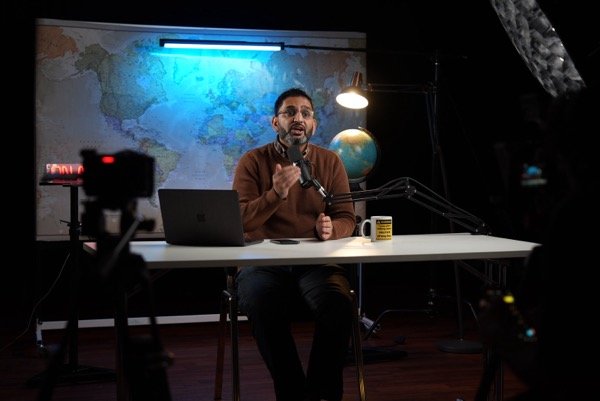 Wide shot of podcast studio recording with multiple cameras and world map